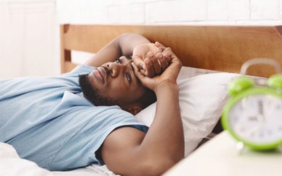 Man lying awake in bed next to alarm clock