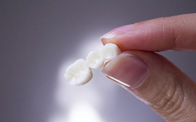 Close-up of fingers holding dental bridge in Wayland, MA