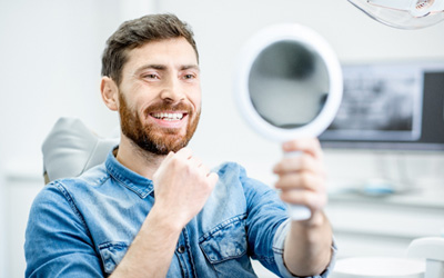 Man sitting in dental chair checking smile in mirror