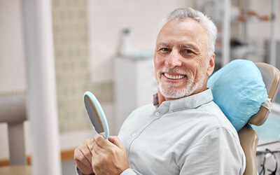 older male dental patient smiling and holding a mirror