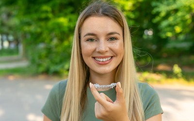 Woman in green shirt holding Invisalign aligner