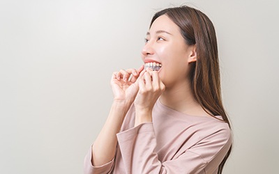 Young woman in light shirt about to wear Invisalign aligner