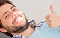 Man leaning back in dental chair and giving thumbs up