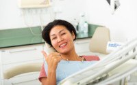 Female dental patient giving thumbs up in chair