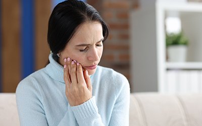 Woman in sweater sitting on couch with jaw pain